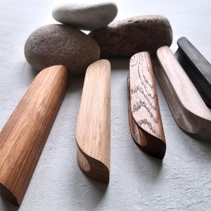 May include: Six wooden cabinet pulls with a variety of finishes, including natural wood, stained wood, and black. The pulls are all approximately 30 cm long and have a curved shape.