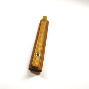 May include: A rectangular wooden handle with a light brown wood grain finish. The handle features two circular silver-colored metal screw inserts positioned along the center line of the top surface, with a small protruding tab at one end.