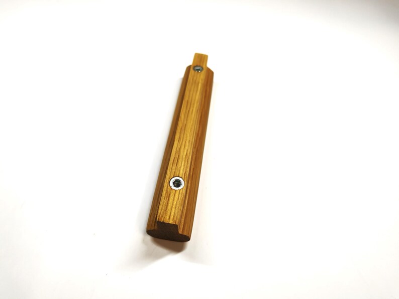 May include: A rectangular wooden handle with a light brown wood grain finish. The handle features two circular silver-colored metal screw inserts positioned along the center line of the top surface, with a small protruding tab at one end.