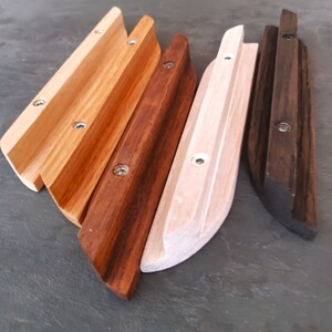 Op de afbeelding: Vier houten wandbeugels voor planken in verschillende houtkleuren. De beugels zijn gemaakt van massief hout en hebben een gebogen vorm. De beugels zijn in de volgende kleuren: naturel hout, donkerbruin, lichtbruin en zwart.