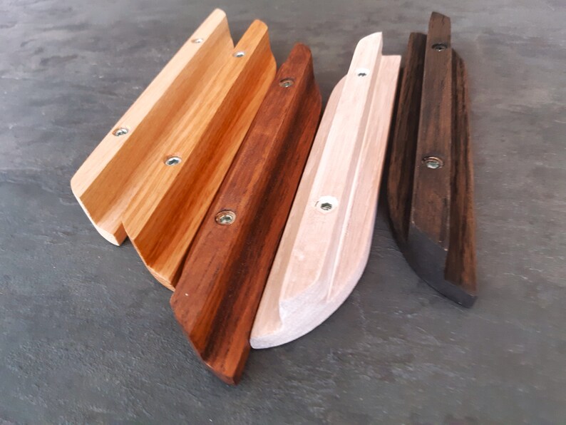 Op de afbeelding: Vier houten wandbeugels voor planken in verschillende houtkleuren. De beugels zijn gemaakt van massief hout en hebben een gebogen vorm. De beugels zijn in de volgende kleuren: naturel hout, donkerbruin, lichtbruin en zwart.