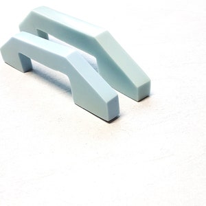 May include: Two light blue plastic cabinet door handles with a modern, geometric design.