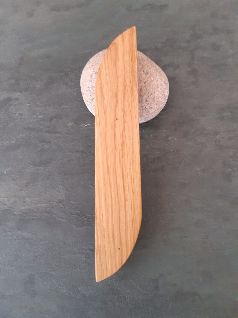 Op de afbeelding: Een houten, lichtbruin, rond, mesvormig object met een glad oppervlak en een licht gebogen rand. Het object ligt op een grijs, getextureerd oppervlak.