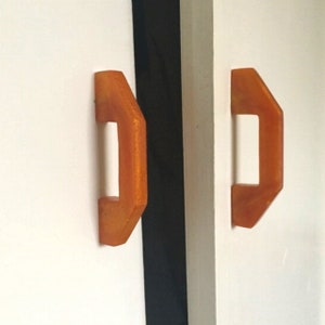 May include: Two orange cabinet door handles with a geometric shape.