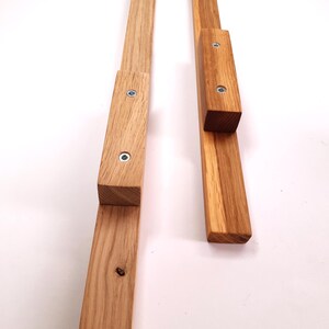 May include: Two wooden wall-mounted coat racks with a simple design. Each rack has a rectangular shape with a small, rectangular shelf attached to the top.
