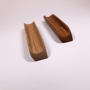 May include: Two wooden, curved, spoon rests made of light brown wood. The rests are similar in shape and size, but one is slightly darker in color.