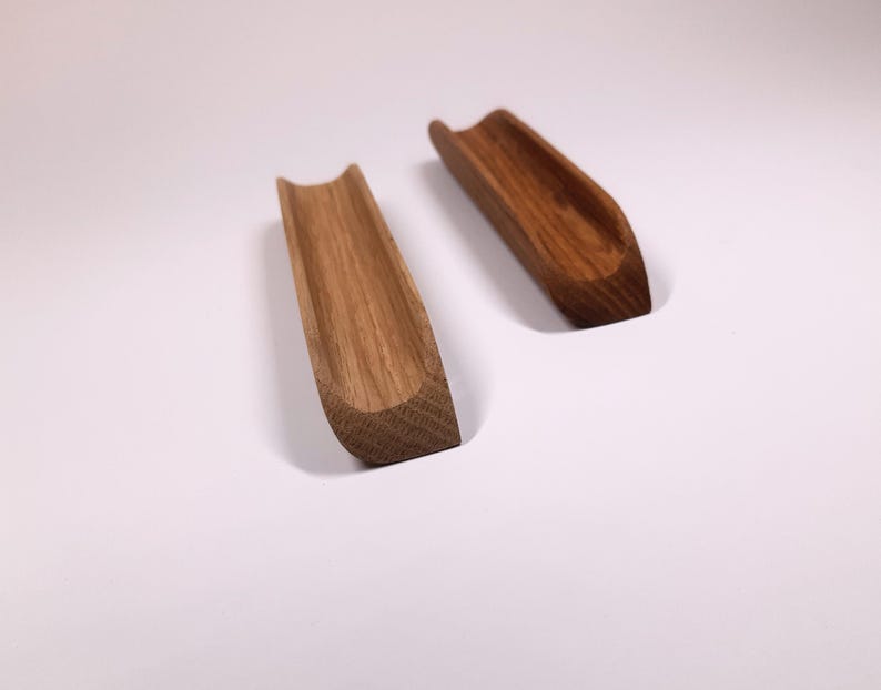 May include: Two wooden, curved, spoon rests made of light brown wood. The rests are similar in shape and size, but one is slightly darker in color.