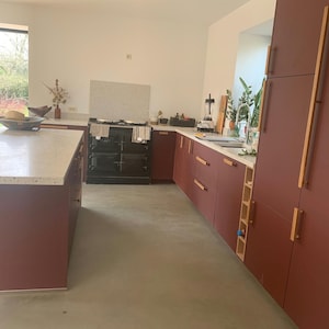 Puede incluir: Una cocina moderna con armarios rojos y un horno negro. Los armarios tienen tiradores de madera y la encimera es blanca con motas negras y grises.