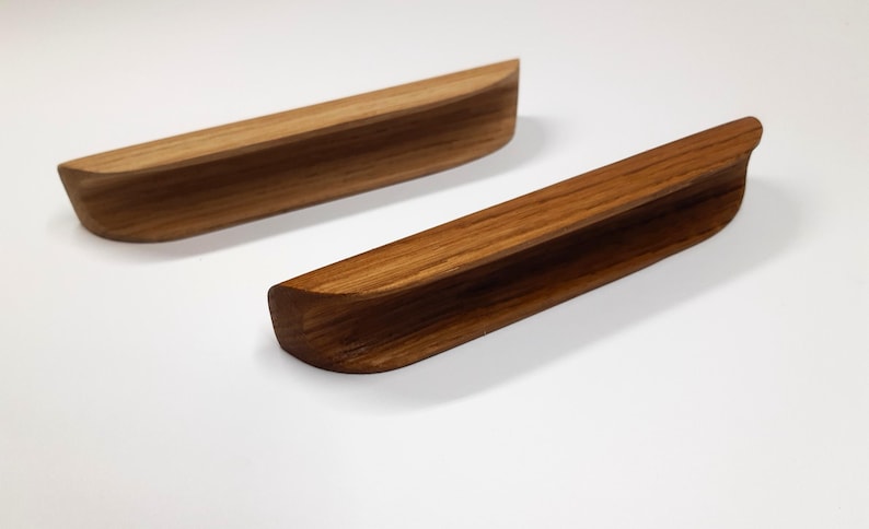 May include: Two wooden drawer pulls with a natural wood finish. The pulls are curved and have a slight lip on the top and bottom.