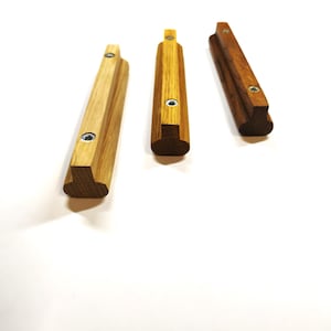 May include: Three elongated wooden cabinet pulls with a T-shaped profile. Each handle features a light to medium brown wood grain finish and two circular metal mounting points with internal threading for attachment to furniture or cabinetry doors.