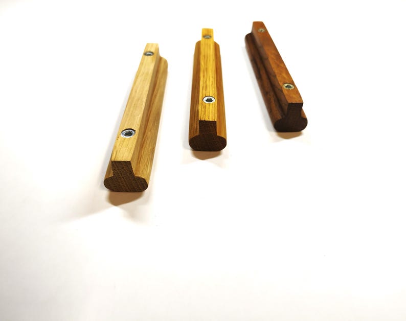 May include: Three elongated wooden cabinet pulls with a T-shaped profile. Each handle features a light to medium brown wood grain finish and two circular metal mounting points with internal threading for attachment to furniture or cabinetry doors.