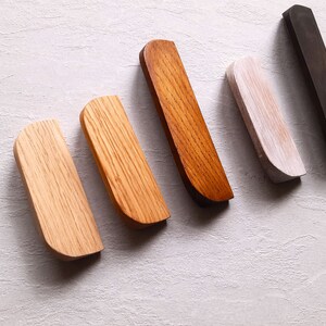 May include: Five wooden drawer pulls in different shades of brown, white, and black. The pulls are all the same shape, with a rounded top and a flat bottom.