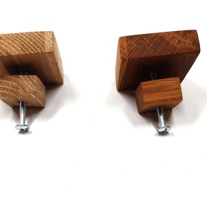 May include: Two square-shaped wooden cabinet knobs with a screw on the bottom. The knobs are made of different shades of wood, one is a light brown and the other is a darker brown.