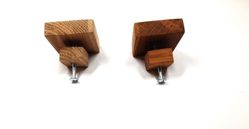 May include: Two square-shaped wooden cabinet knobs with a screw on the bottom. The knobs are made of different shades of wood, one is a light brown and the other is a darker brown.
