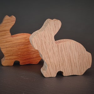 May include: Two wooden rabbit figurines, one is a light brown colour and the other is a darker brown colour. Both are carved in a simple, stylised shape.