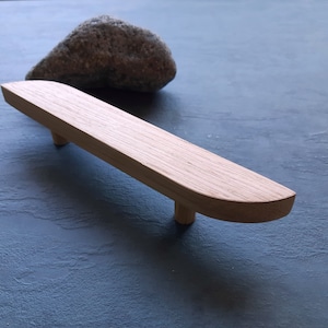 Könnte beinhalten: Ein Holz-Schrankgriff mit abgerundeter, leicht geschwungener Form. Der Griff ist aus hellem Holz gefertigt und hat ein schlichtes, minimalistisches Design.