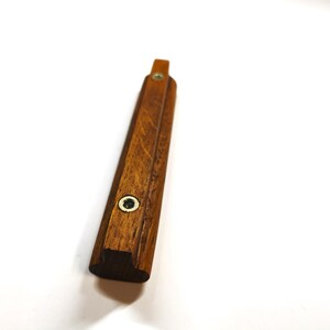 May include: A long, rectangular wooden handle with a rich brown grain pattern. The handle features two circular metal inserts with screw holes positioned along its length, providing a secure mounting point for attachment to a cabinet or drawer.