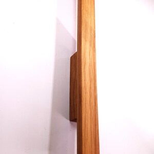 May include: A wooden wall sconce with a natural wood finish. The sconce has a rectangular shape and is mounted to the wall with a small, rectangular bracket.