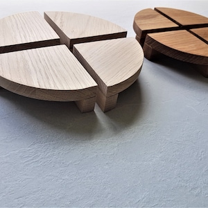 Op de afbeelding: Twee houten serveerschalen, elk bestaande uit vier gebogen delen. Eén is licht van kleur, de andere donkerder bruin. Beide hebben kleine, vierkante voetjes. De schalen staan op een lichtgrijze ondergrond.