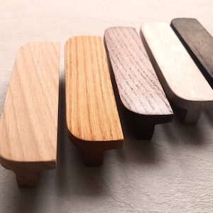 Könnte beinhalten: Sechs Holzknaufgriffe in verschiedenen Brauntönen, von hell bis dunkel, mit abgerundeten Kanten und einer leicht geschwungenen Form.