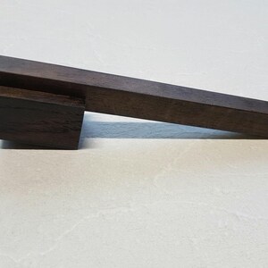 Puede incluir: Un tirador de madera marrón oscuro de forma rectangular. El tirador está hecho de dos piezas de madera, una encima de la otra.
