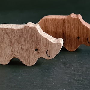 Peut inclure: Deux figurines de rhinocéros en bois, l'une brun clair et l'autre brun foncé, avec des yeux et des bouches peints en noir. Les figurines sont sculptées avec un motif de grain de bois.