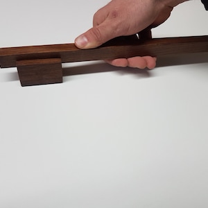 Può includere: Una maniglia per armadio in legno marrone scuro con una base quadrata e una barra rettangolare. La maniglia è realizzata in legno massello e ha una finitura liscia.