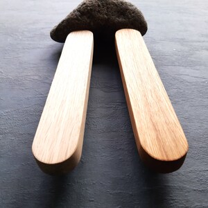 Op de afbeelding: Twee houten stokken met afgeronde uiteinden, rechtop geplaatst en een donkergrijze steen ondersteunend.