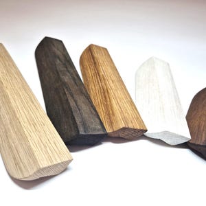 May include: Five wooden cabinet pulls of varying lengths and finishes arranged in a row. The pulls feature a faceted, angular design with pointed ends. The colors range from light natural oak to medium brown, dark espresso, and a painted white finish.