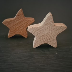 May include: Two wooden star-shaped ornaments. One is a light brown color, and the other is a darker brown. The stars have a rustic, natural wood grain appearance. They are likely handmade and suitable for home decor.