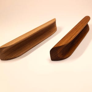 May include: Two wooden drawer pulls with a curved design. The pulls are made of natural wood and have a light brown color.