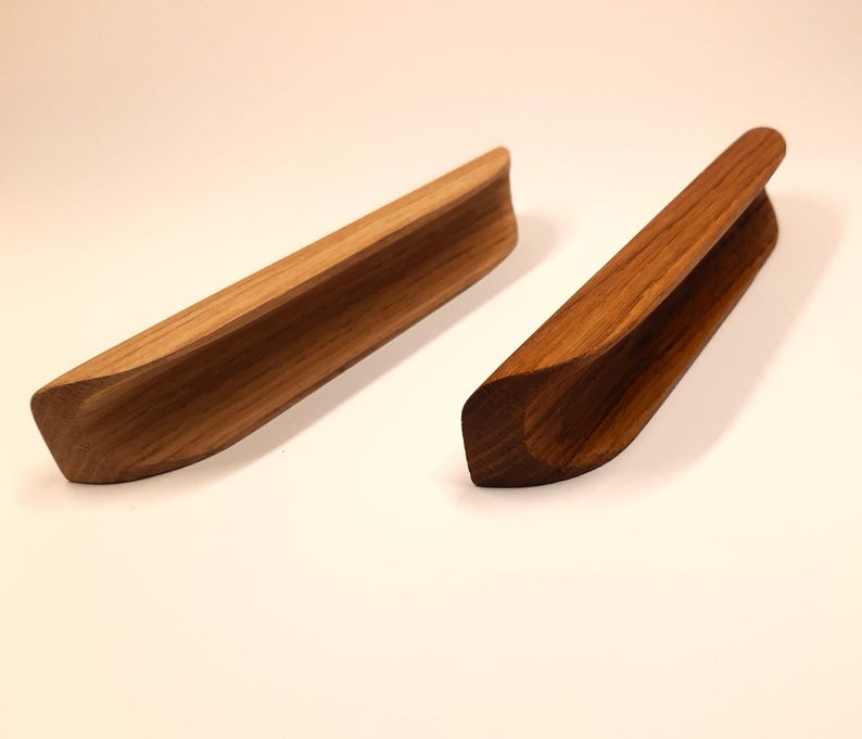 May include: Two wooden drawer pulls with a curved design. The pulls are made of natural wood and have a light brown color.