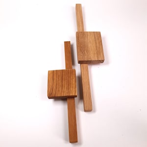 Könnte beinhalten: Zwei Holzlineale mit quadratischen Enden. Die Lineale sind aus hellbraunem Holz gefertigt und in Kreuzform angeordnet.