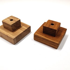 May include: Two wooden display stands with a square base and a smaller square block on top. Both blocks have a small hole in the centre.