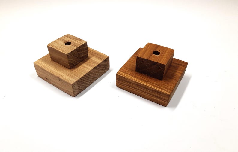 May include: Two wooden display stands with a square base and a smaller square block on top. Both blocks have a small hole in the centre.