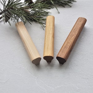 Puede incluir: Tres pomos de madera para armario en diferentes tonos de marrón. Los pomos son cilíndricos con la parte superior redondeada y la inferior puntiaguda.