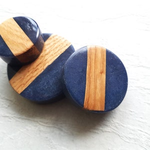 Peut inclure: Trois jauges d'oreille rondes en bois et résine avec un motif bleu et grain de bois. Les jauges sont empilées les unes sur les autres.