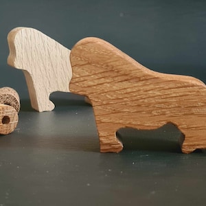 May include: Two wooden animal figurines, one a brown bull and the other a light brown bear, are arranged on a dark surface. The bull is standing with its head turned to the side, while the bear is lying down with its head resting on its paws. There are also two small wooden cylinders on the surface.