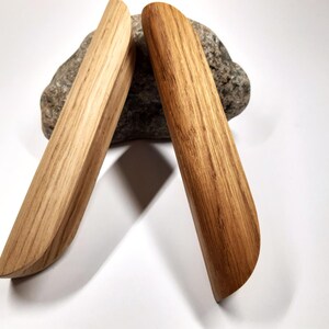 May include: Two wooden handles with a rounded, slightly curved shape. The handles are made of light brown wood with a natural grain pattern.