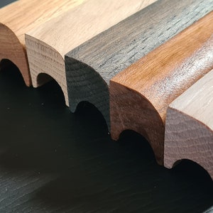 May include: Five wooden trim pieces with rounded edges in different shades of brown, including light brown, dark brown, and black.