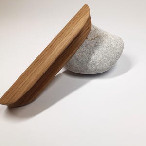 May include: A wooden drawer pull with a rounded edge and a natural wood finish.