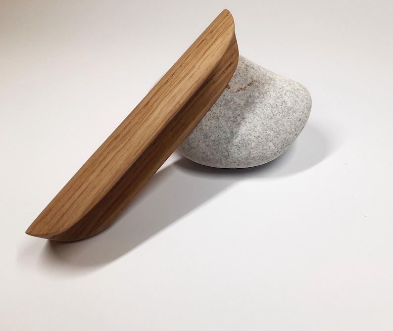 May include: A wooden drawer pull with a rounded edge and a natural wood finish.