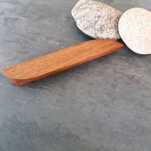 Op de afbeelding: Een houten kastgreep met een afgeronde rand en een natuurlijke houten afwerking.