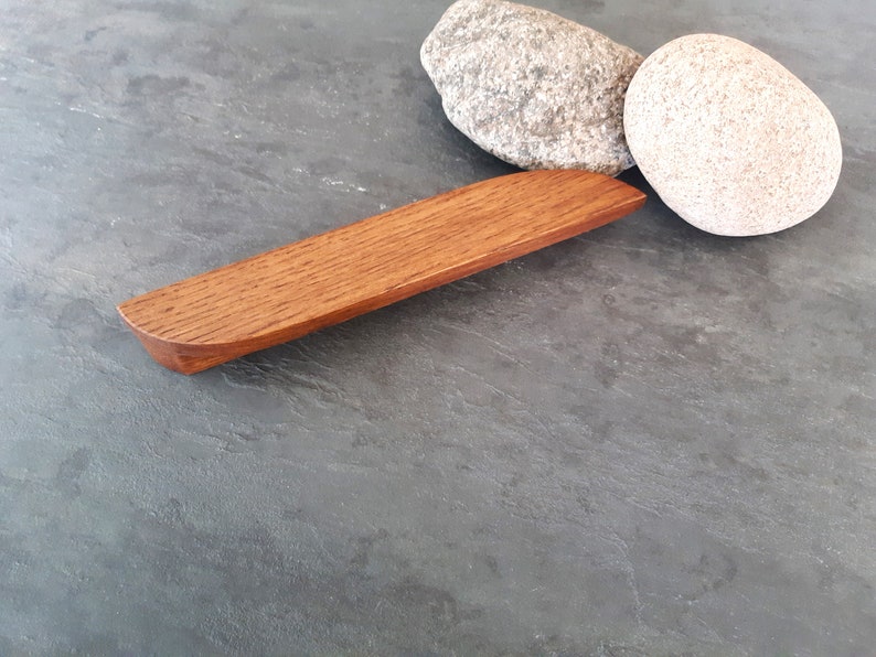 Op de afbeelding: Een houten kastgreep met een afgeronde rand en een natuurlijke houten afwerking.