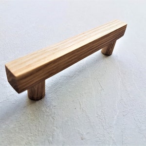May include: A wooden cabinet pull with a rectangular shape and a natural wood finish.