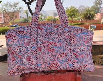May include: A pink and blue floral print duffel bag with two top handles. The bag is made of cotton fabric and has a traditional Indian design.