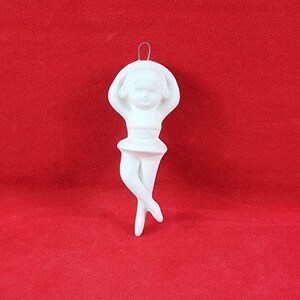 May include: White ceramic ornament of a ballerina with her arms raised above her head. The ornament is designed to hang from a Christmas tree.