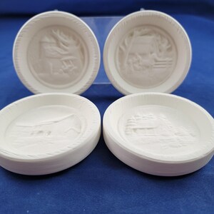 May include: Four white, round, ceramic dishes with embossed landscape scenes. Each dish features a different design, including a house, trees, and a bridge. The dishes have a textured, ridged edge and are displayed on a blue surface.