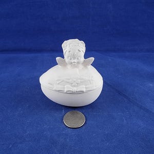 May include: White ceramic egg-shaped trinket box with a small angel figurine on top. The angel has wings and a floral wreath around its head. The egg is decorated with a floral design and a bow.