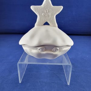 May include: White ceramic clam shell trinket box with a starfish lid. The starfish has a smiling face and textured surface.